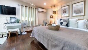 A bedroom with a bed, a desk, a chair, a standing fan, a TV, and framed pictures on the wall. - Jasmine Garden Bungalow (Koh Samui)