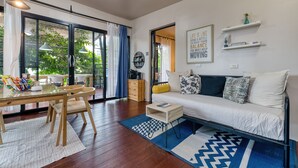 A modern living room with a sofa, a dining table with chairs, a coffee table, and a view of greenery outside. - Jasmine Garden Bungalow (Koh Samui)