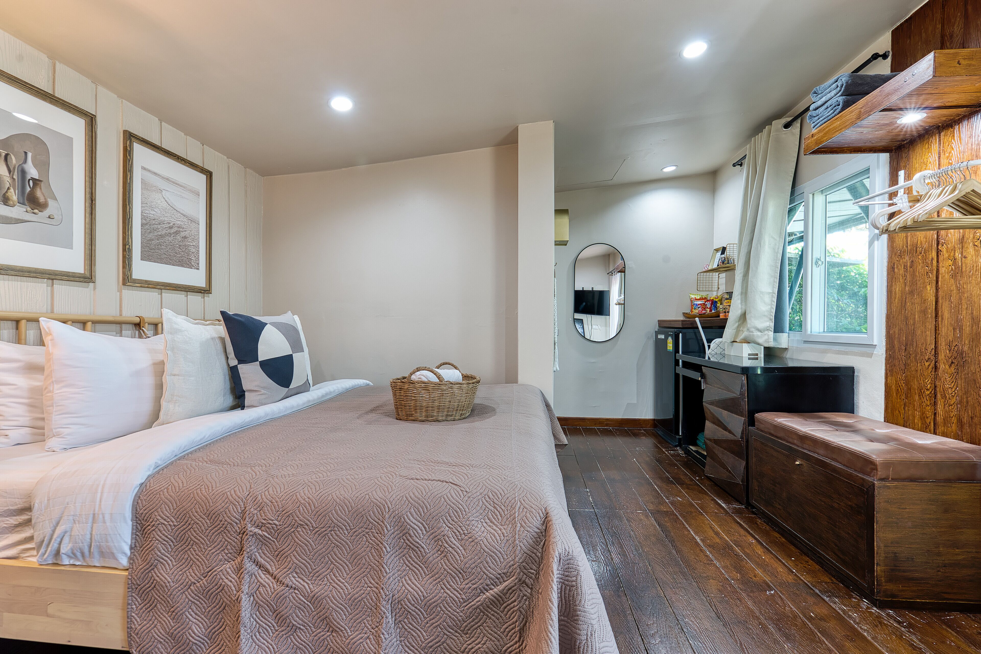 A bedroom with a bed, a wooden bench, a wicker basket, a mirror, and a window with curtains.