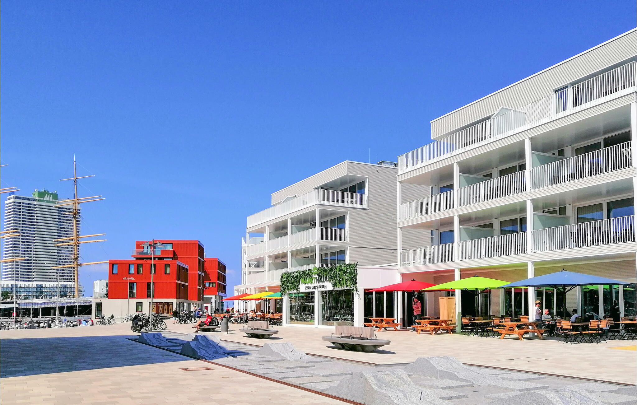 Une place urbaine moderne, dotée d’un espace extérieur aménagé et offrant une vue sur le bord de l’eau.