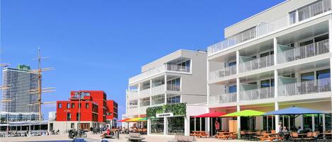 Une place urbaine moderne, dotée d’un espace extérieur aménagé et offrant une vue sur le bord de l’eau.