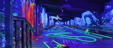 A neon-lit pathway with digital displays on the walls, a wooden deck, and a ceiling with lighting fixtures.