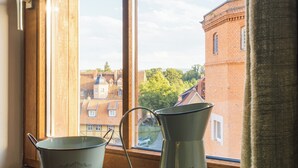 Two flower pots on a windowsill with a view of a brick building and trees.