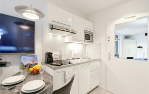 A modern kitchen with white cabinets, a microwave, a coffee maker, and a sink. There is a television on the left and a door with a mirror on the right.