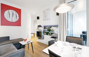 A modern living room with a flat-screen TV, a dining area with white tableware, and a red abstract painting on the wall.