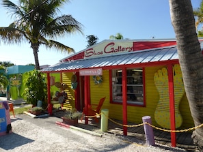 Une petite boutique de chaussures aux couleurs vives, avec une façade rouge et jaune, une enseigne indiquant « Merrell » et une vitrine présentant des chapeaux et des chaussures à l’extérieur.