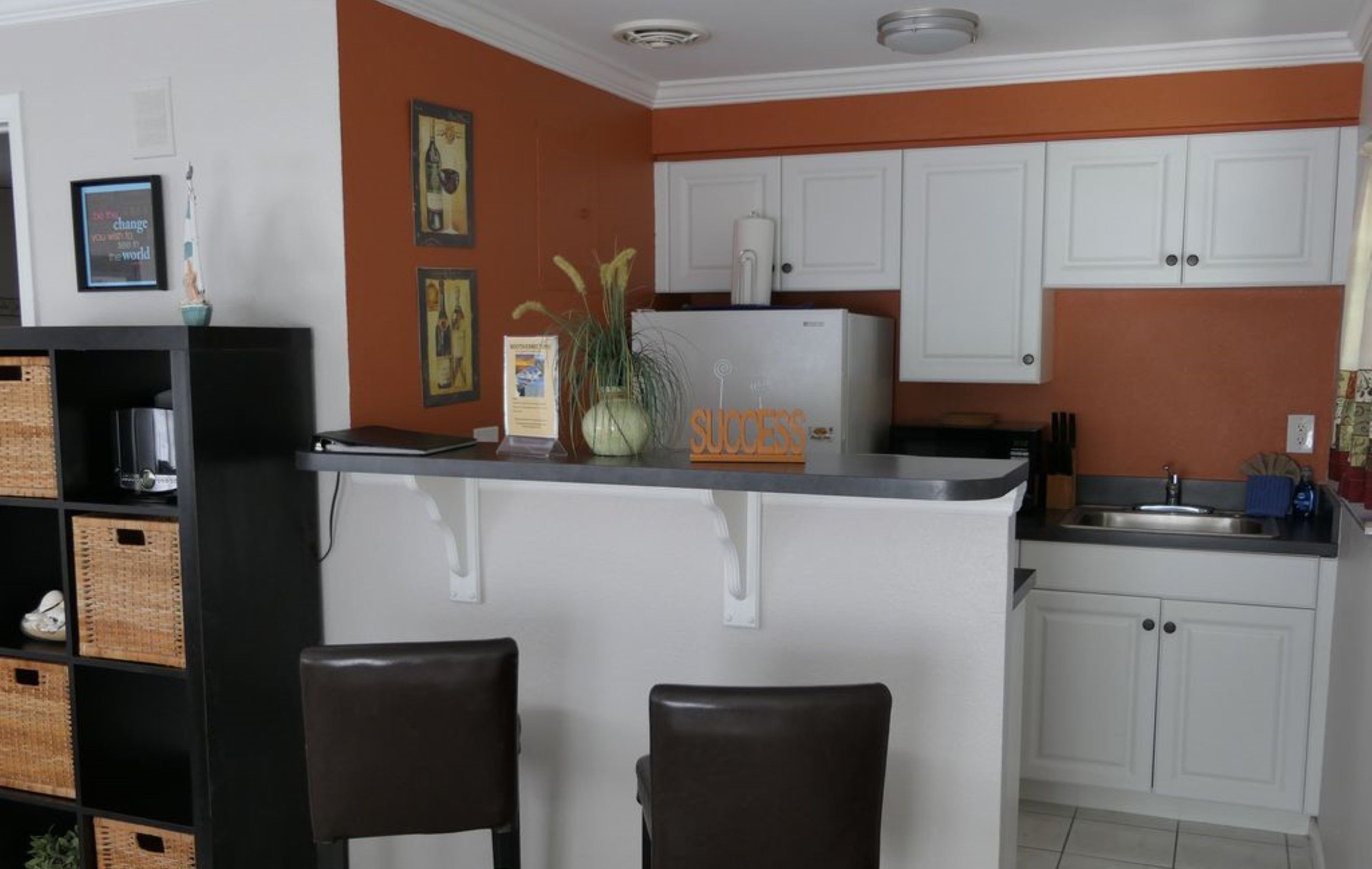 A kitchen with white cabinets, a black countertop, and two bar stools.