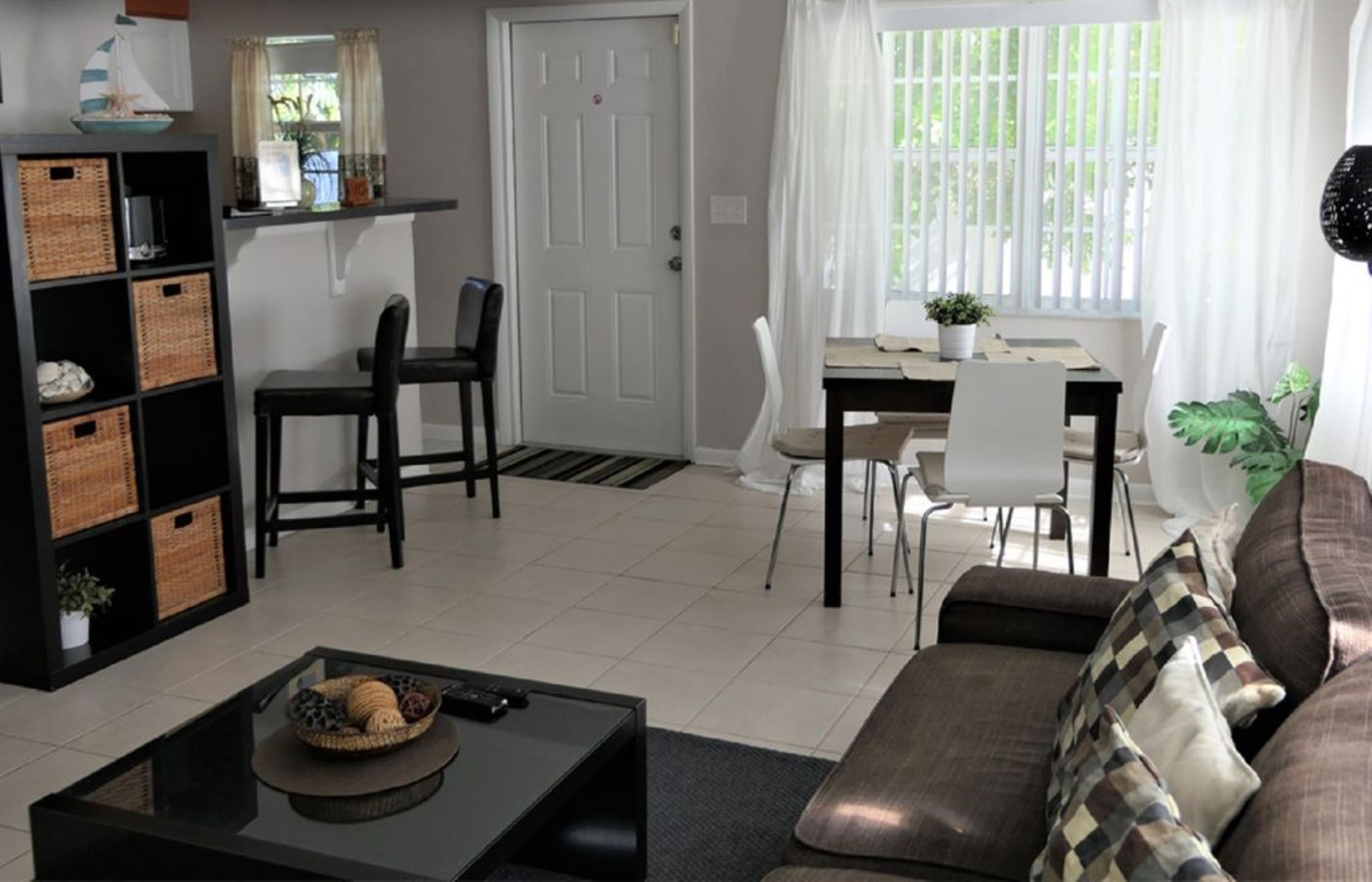 A living room with a sofa, a coffee table, a dining area with a table and chairs, a ceiling fan, and a door.