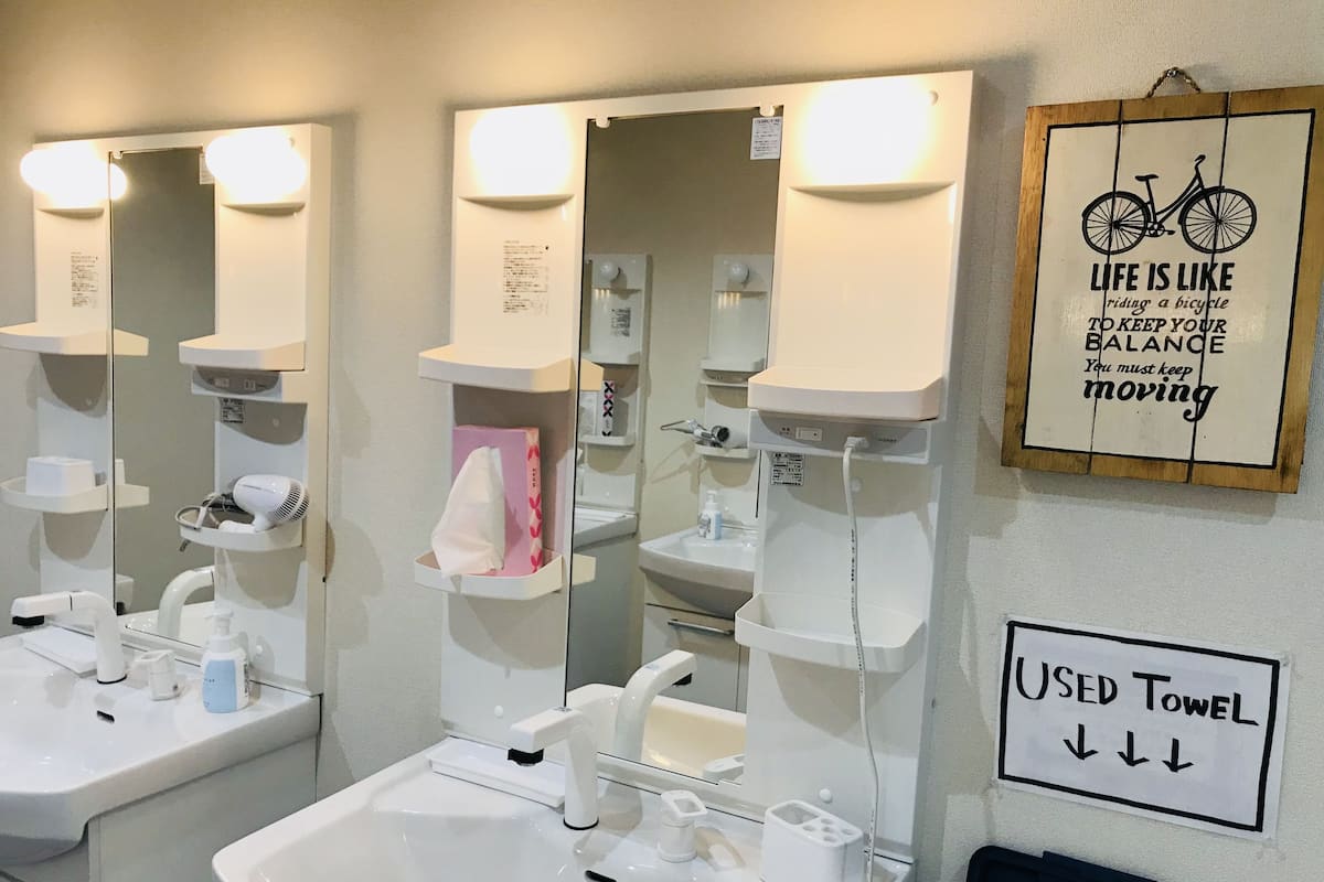 A bathroom with two sinks, mirrors, and a towel rack. There are signs indicating towel usage and a motivational quote about life.
