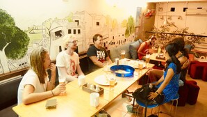 A group of people seated around a table in a restaurant with a mural on the wall. - ONE Hostel&Standing Bar (Himeji)