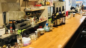 A kitchen with a wooden counter, various kitchen appliances, and shelves with bottles and glasses. - ONE Hostel&Standing Bar (Himeji)