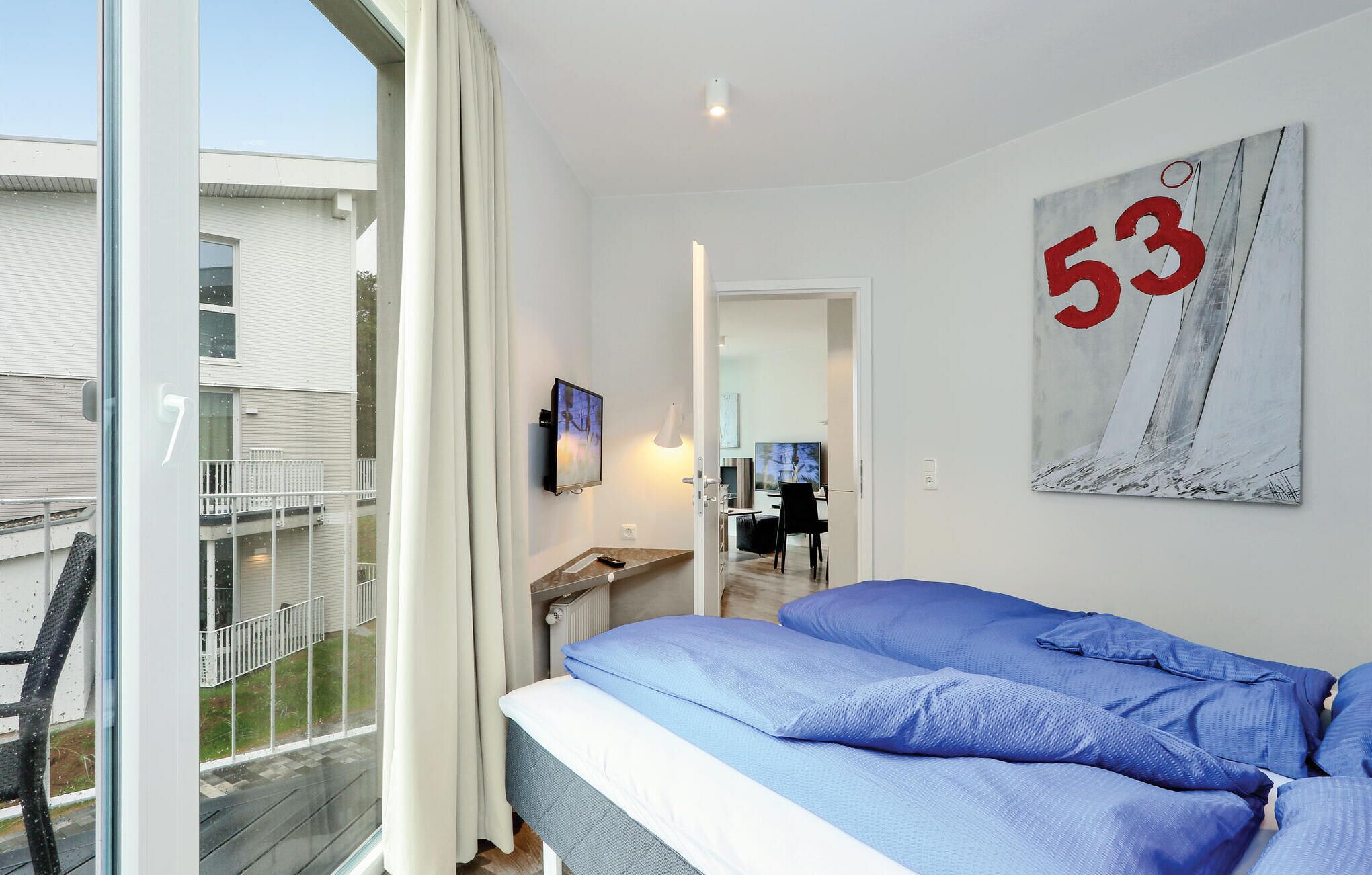 Ein modernes Schlafzimmer mit einem großen Bett, einem an der Wand montierten Fernseher und einem Balkon mit Geländer.