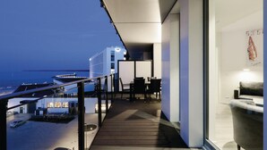 A balcony with a view of the sea, a dining area with chairs and tables, and a modern building in the background. - HighEnd Travemünde - Whg 507 (Lübeck Travemünde)