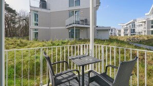 Un balcon doté de meubles en osier et d’une table, offrant une vue sur un quartier résidentiel avec des immeubles modernes.