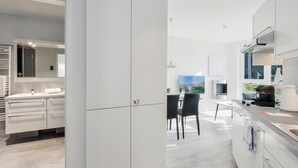 Une cuisine moderne avec des meubles blancs, un coin repas avec deux chaises noires et une grande fenêtre offrant une vue sur l’extérieur.
