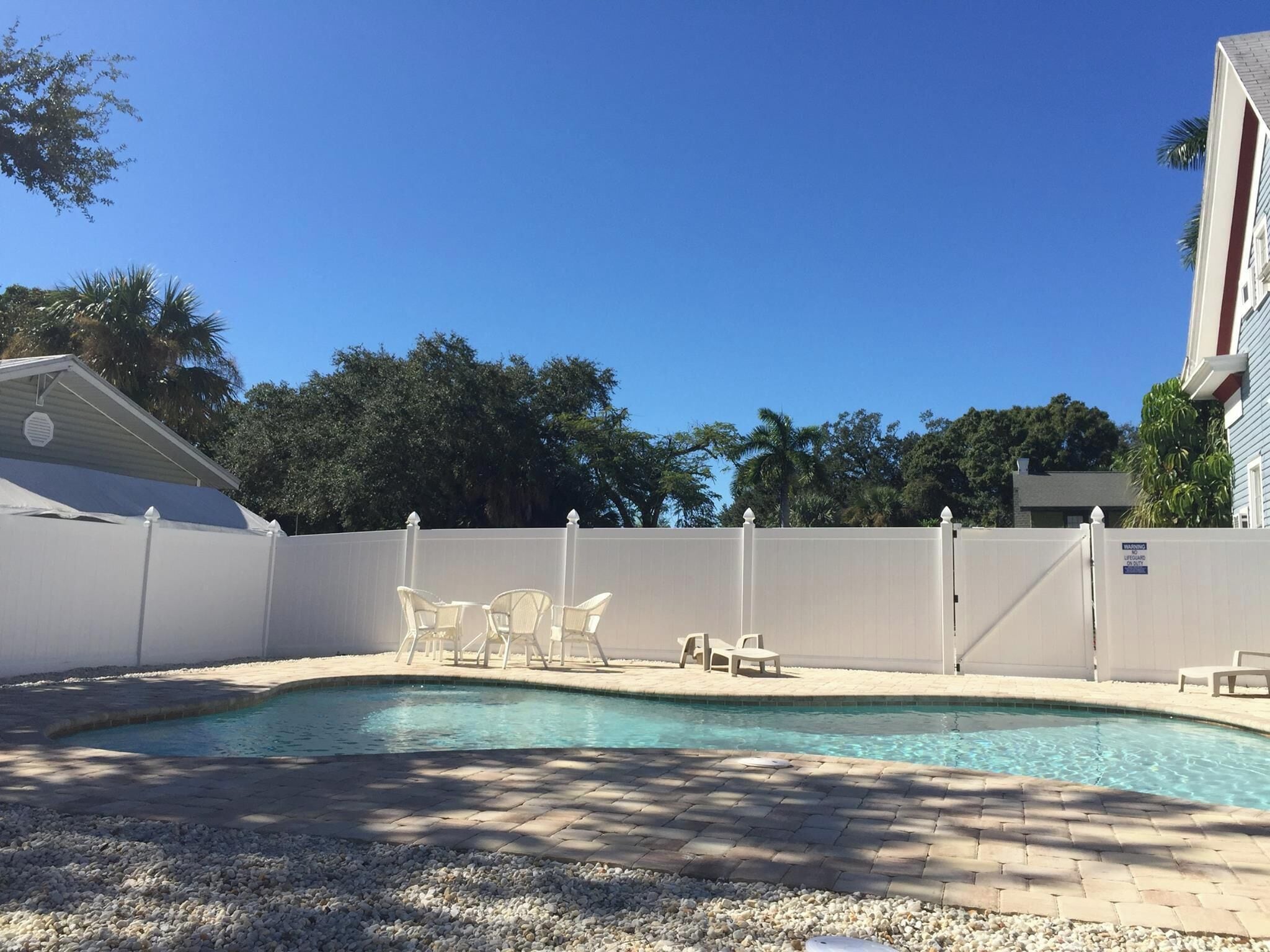 A swimming pool with lounge chairs and a white fence.