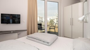 Une chambre d’hôtel avec un lit, un téléviseur fixé au mur, une porte-fenêtre coulissante donnant sur un balcon et une armoire.