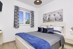 Una camera da letto moderna con un letto grande, una finestra con tende, un quadro e un comodino.