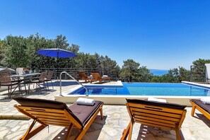 Area piscina con lettini e tavolo, con vista su un cielo azzurro e sul mare.
