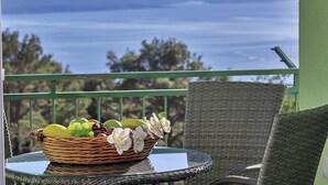 A wicker chair and table with a fruit basket and flowers on a balcony overlooking a body of water. -  Holiday house with heated pool, terrace with sea view, 3 bedrooms, WiFi, BBQ (Bast)