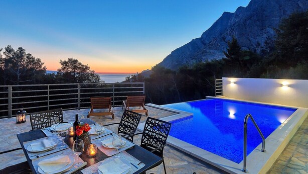 An outdoor dining area with a pool, overlooking a mountainous landscape at sunset. -  Holiday house with heated pool, terrace with sea view, 3 bedrooms, WiFi, BBQ (Bast)