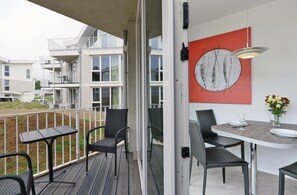Een balkon met zitplaatsen buiten, een eethoek met stoelen en een tafel, en uitzicht op aangrenzende gebouwen.