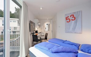 Een moderne hotelkamer met een balkon, een zithoek en een keuken, zichtbaar door een geopende deur.