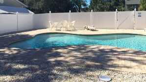 A swimming pool with a white fence, a covered patio area, and outdoor furniture.