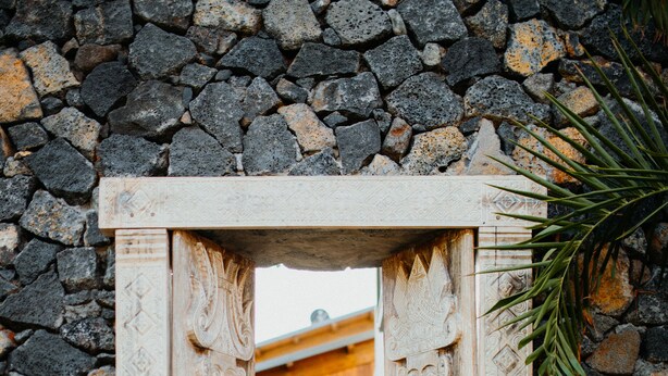 Une porte en bois sculptée, ornée de motifs complexes, qui se détache sur un mur de pierre.