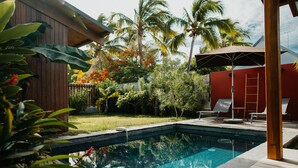 Une piscine dotée d’une terrasse en bois, entourée d’une végétation luxuriante et de palmiers.
