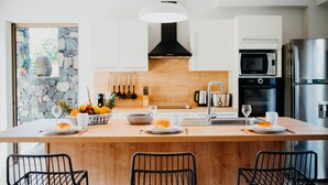 Une cuisine moderne dotée d’un îlot central, de meubles blancs, d’un pare-feu en pierre et d’appareils électroménagers en acier inoxydable.
