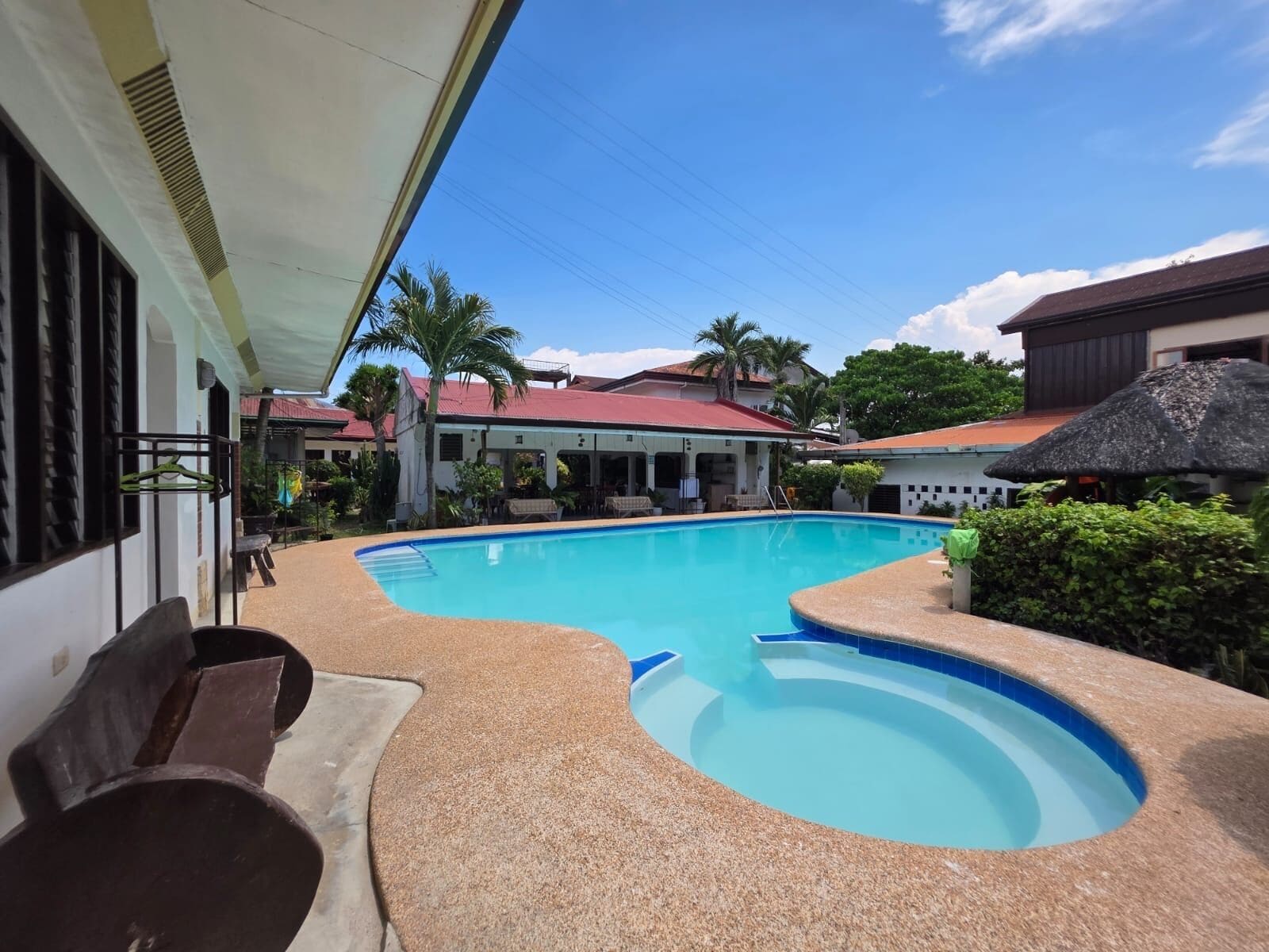 A swimming pool with a curved design, surrounded by a covered area with benches.
