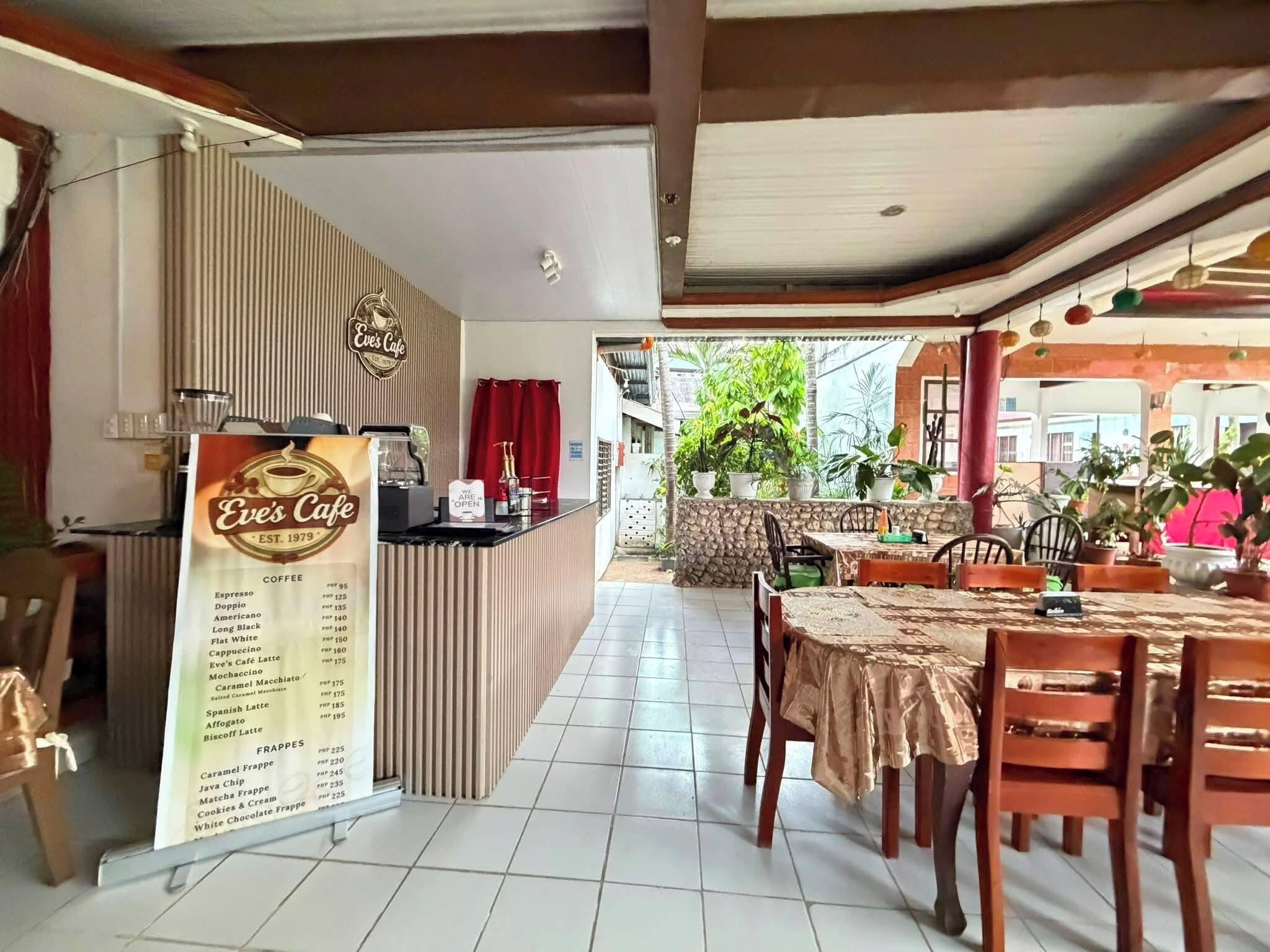 Una cafetería con una pizarra de menú, mesas al aire libre y plantas en macetas.