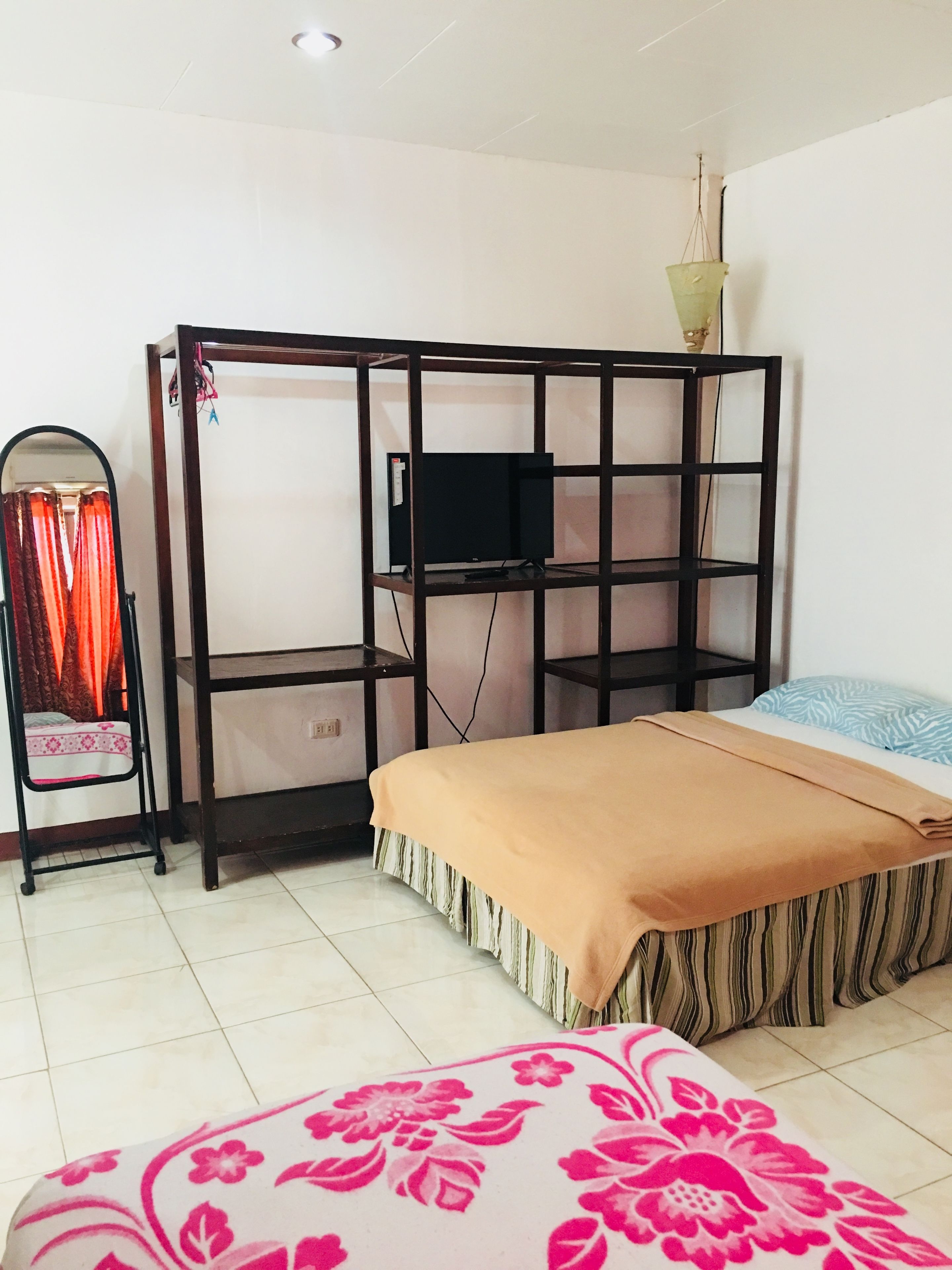 A bedroom with a bunk bed, a small desk with a television, a chair, and a bed with a patterned bedspread.
