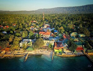 An aerial view of a coastal town with houses, a pier, and a lighthouse in the background. - New Eve's Kiosk Dive Resort (Moalboal)