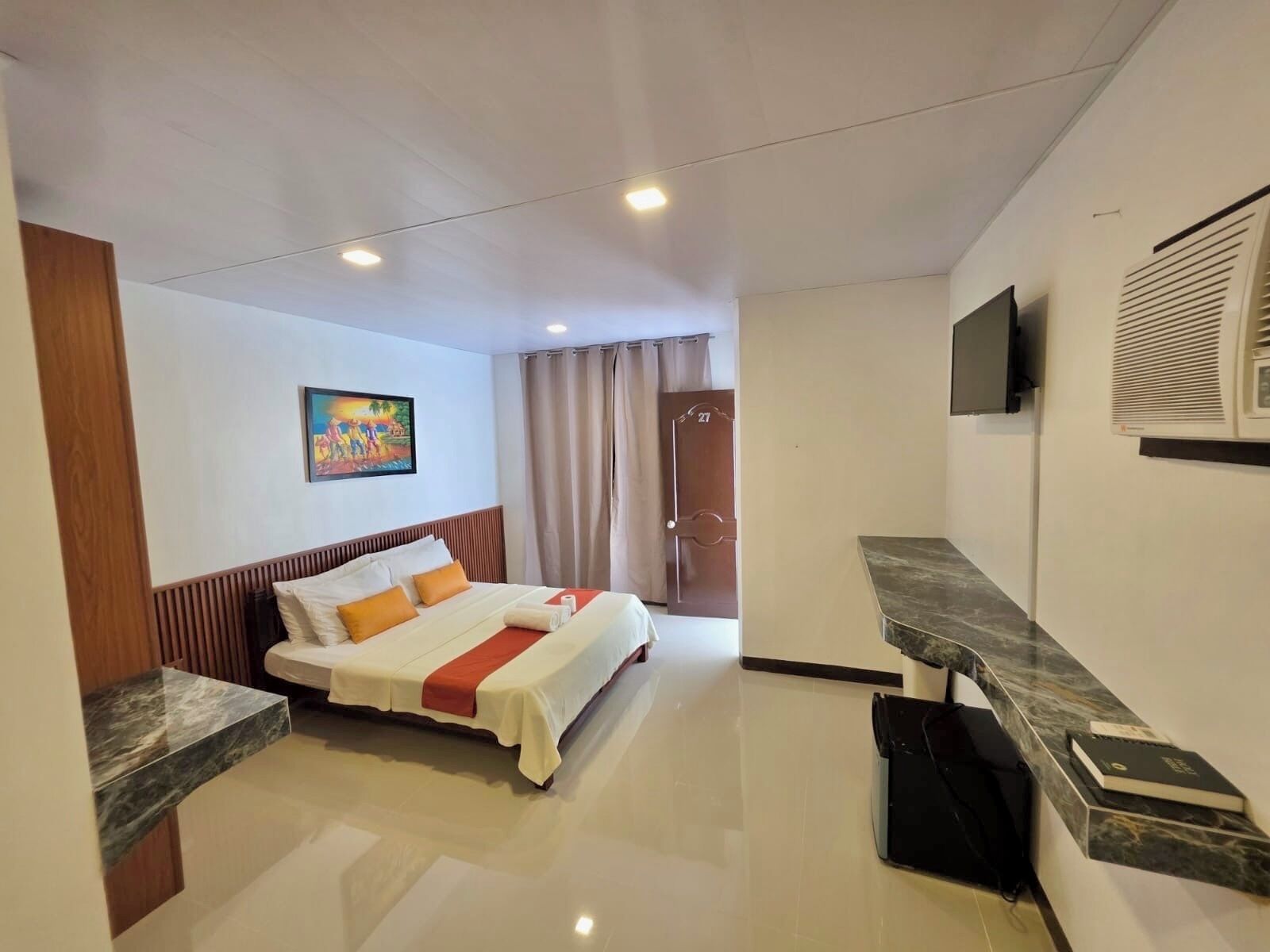 A hotel room with a bed, a desk, a TV, and a painting on the wall.