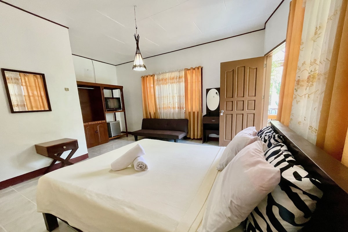 Habitación de hotel con cama, escritorio, televisor, armario y puerta que da a un balcón.