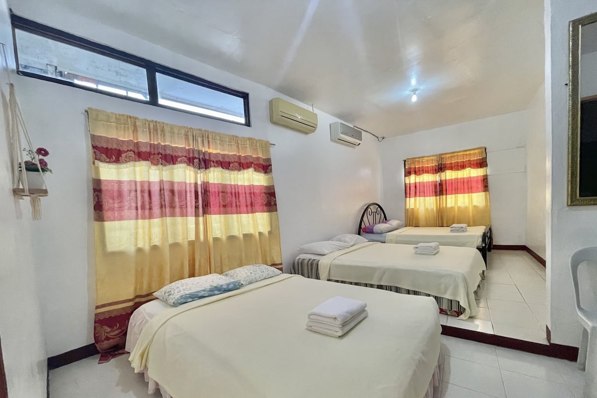Habitación de hotel con dos camas, una ventana con cortinas, un equipo de aire acondicionado y una pequeña mesa con una silla.