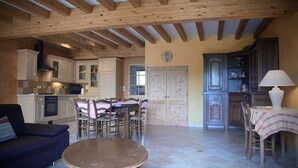 A spacious living area with a dining table, chairs, a sofa, and a kitchen with wooden cabinets and a stove. - Gites le Paradis *** Superb view of Vercors (Pont-en-Royans)