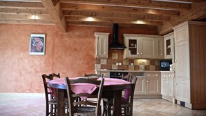 A dining area with a wooden table and chairs, a kitchen with cabinets and appliances, and a framed picture on the wall. - Gites le Paradis *** Superb view of Vercors (Pont-en-Royans)