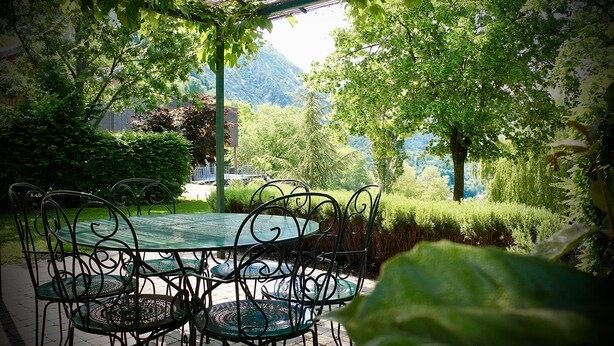 An outdoor seating area with a round table and chairs, surrounded by greenery and trees. - Gites le Paradis *** Superb view of Vercors (Pont-en-Royans)