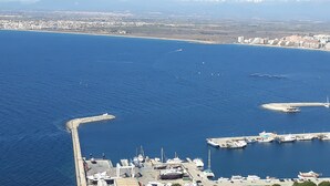 Een kustjachthaven met aangemeerde boten, een steiger die in het water uitloopt, en een stadsgezicht met bergen op de achtergrond.