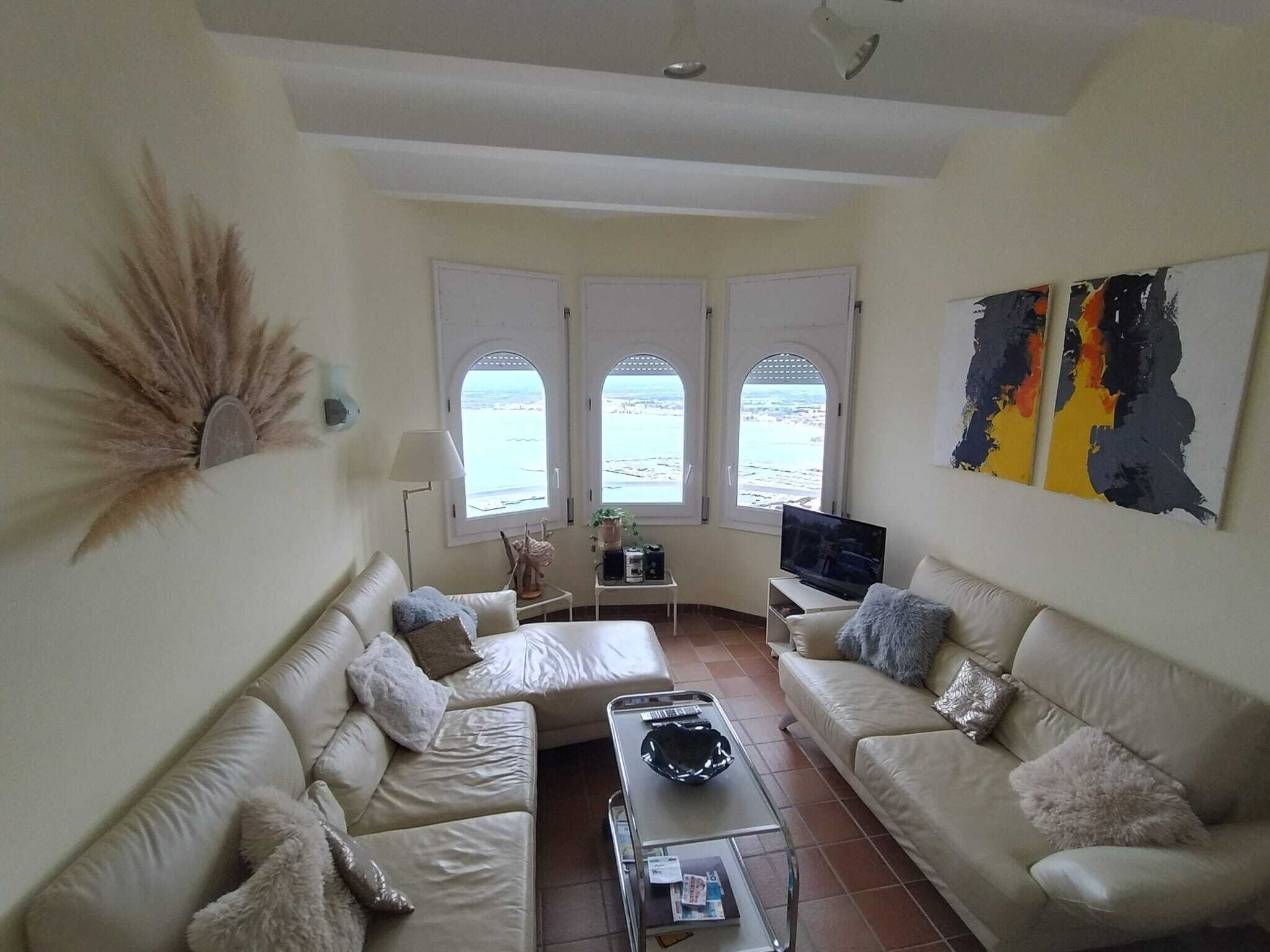 A living room with two sofas, a coffee table, a TV, and a view through arched windows.