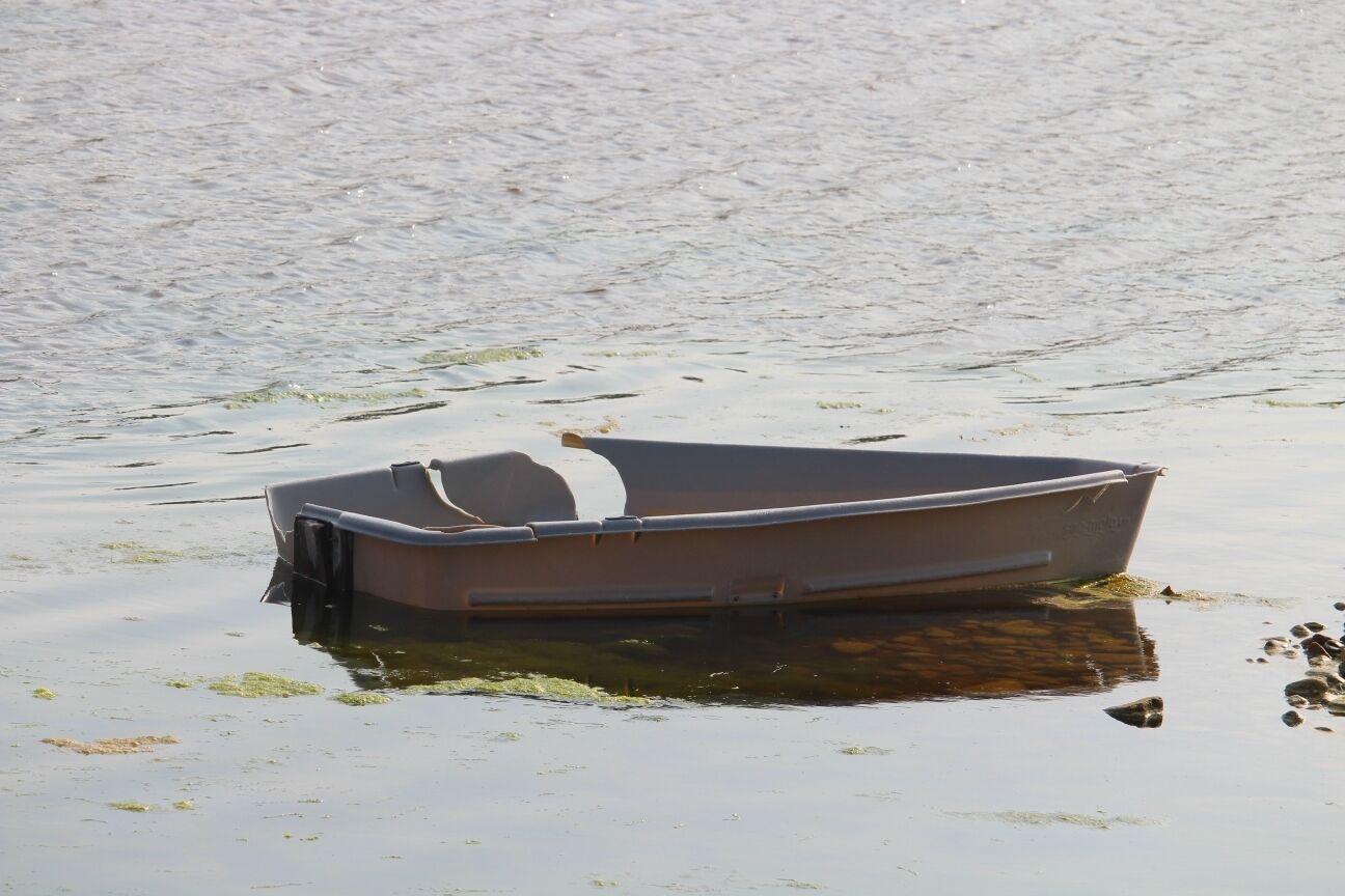 Een klein, stilstaand bootje op kalm water met wat drijvende objecten.