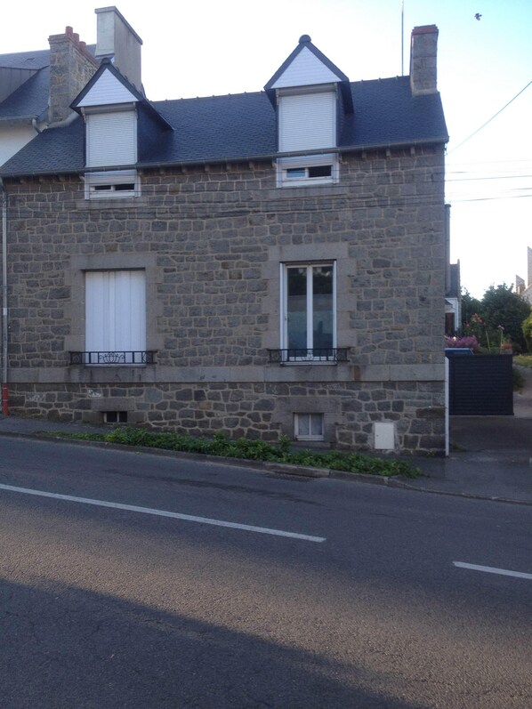 A stone building with a gabled roof, two windows with shutters, and a small balcony.
