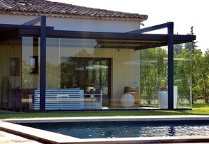 A modern house with a glass-enclosed patio, a pool, and a well-maintained garden.
