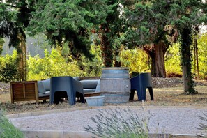 A garden area with outdoor furniture, including a bench and chairs, surrounded by trees and a gravel path.