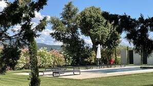 A poolside area with benches and a covered seating area, surrounded by trees and flowering bushes. - Haven of peace in the vineyards (Violes)