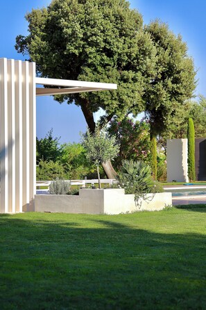 A modern outdoor area with a pergola, a large tree, and a well-maintained lawn.