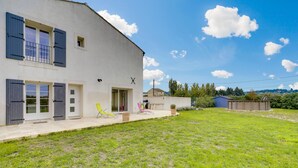 Une maison à deux étages avec une grande pelouse devant, un petit patio avec des meubles d’extérieur et un garage.